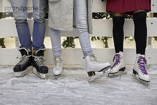 Beine von Freunden mit Schlittschuhen  die an einer Eisbahn stehen