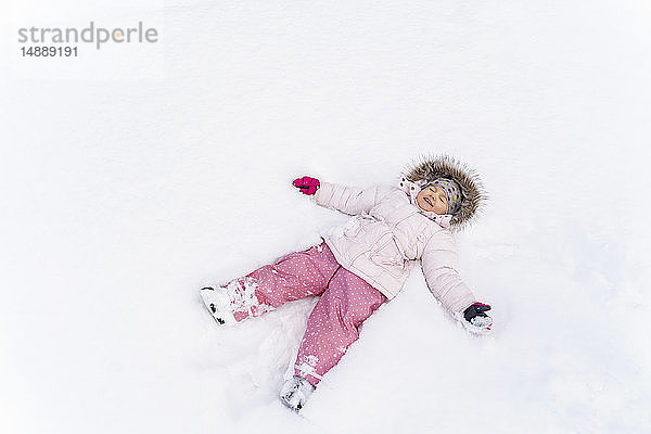 Süßes kleines Mädchen liegt im Winter im Schnee und macht einen Schneeengel