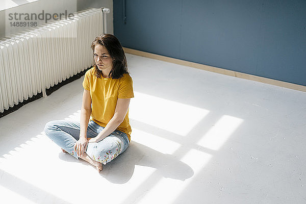 Nachdenkliche Frau sitzt im Sonnenlicht im Schneidersitz auf dem Boden