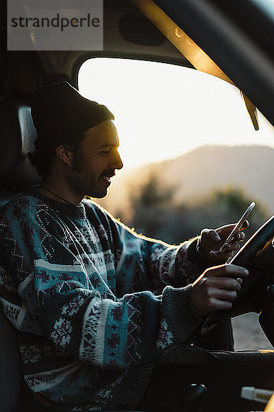 Junger Mann auf einer Autoreise mit einem Smartphone