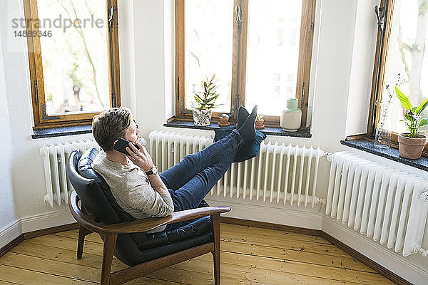 Lässiger Mann sitzt in Lounge Chair in stilvoller Wohnung und telefoniert