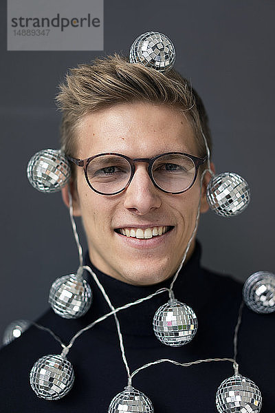 Porträt eines lächelnden jungen Mannes mit Spiegelkugel-Lichterkette