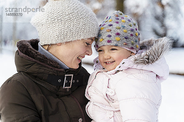 Glückliche  liebevolle Mutter trägt Tochter im Winter