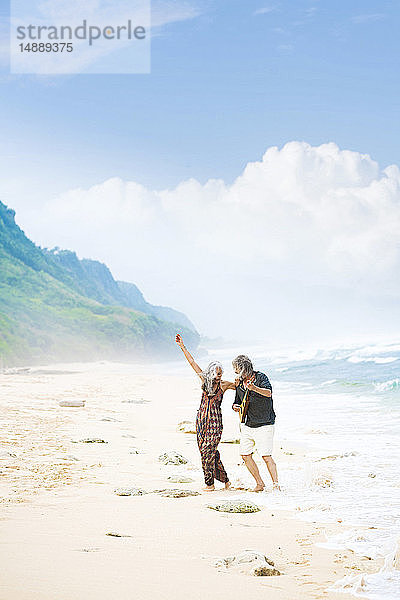 Glückliches älteres Hippie-Paar mit Gitarre tanzt am Strand