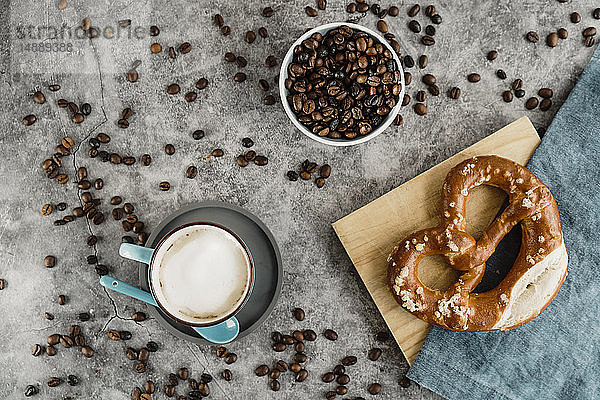Tasse mit weissem Kaffee  Kaffeebohnen und Brezel auf Serviette und Holzbrett