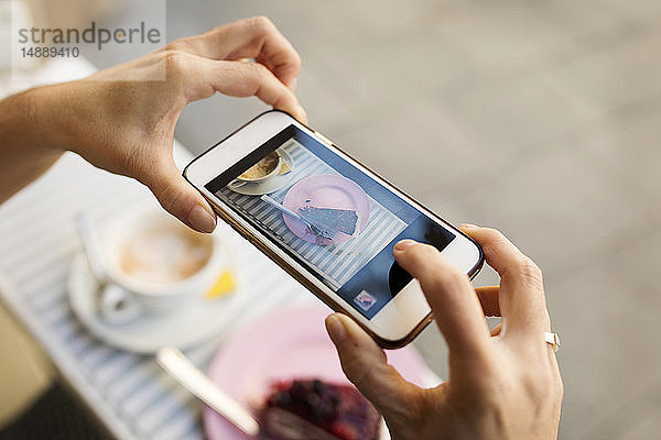 Frauenhände fotografieren ein Stück Kuchen mit einem Smartphone