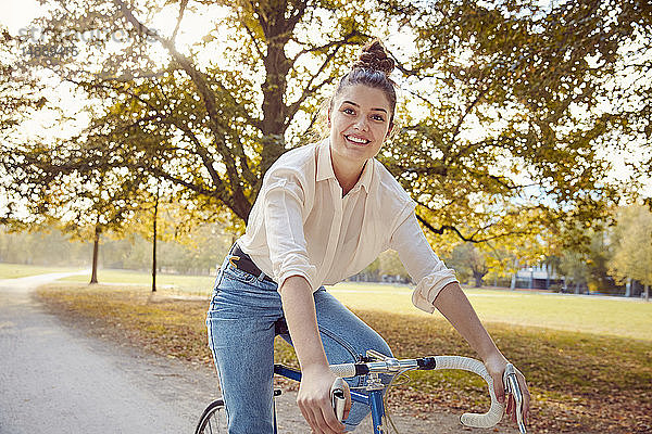 Porträt einer lächelnden jungen Frau beim Fahrradfahren in einem Park