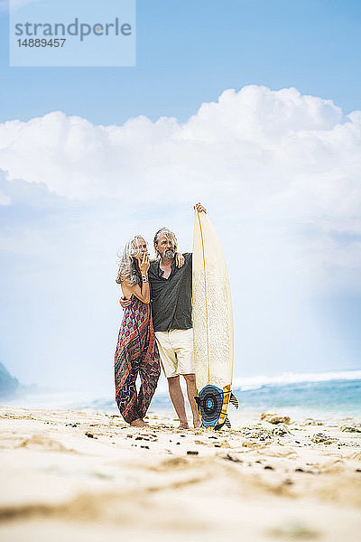 Älteres Hippie-Paar steht mit Surfbrett am Strand
