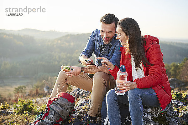 Glückliches Paar auf einer Wanderung in den Bergen macht eine Pause und schaut auf sein Handy