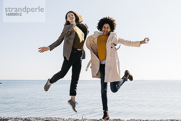 Zwei glückliche Freunde springen am Strand und genießen ihre Freizeit