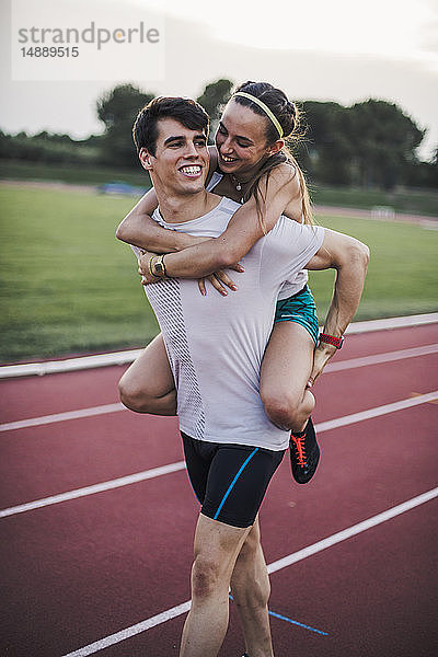 Glücklicher Athlet  der seine Freundin huckepack auf einer Tartanbahn mitnimmt
