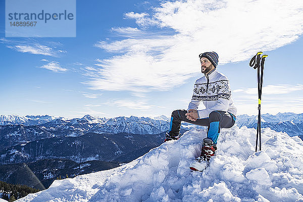 Deutschland  Bayern  Brauneck  Mann im Winter auf Berggipfel sitzend