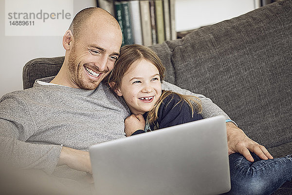 Vater und Tochter sitzen auf der Couch und benutzen einen Laptop