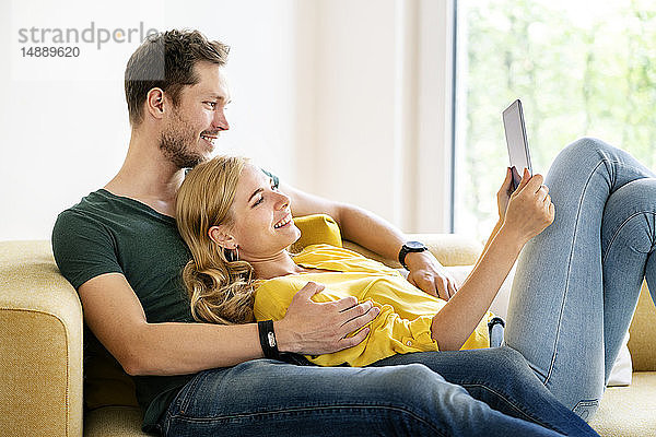 Paar  das in seinem neuen Zuhause auf der Couch sitzt und ein digitales Tablet benutzt