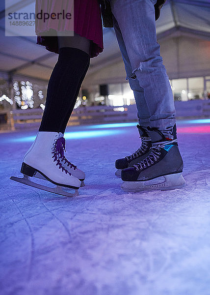 Beine eines Schlittschuh tragenden Paares  das auf einer Eisbahn steht