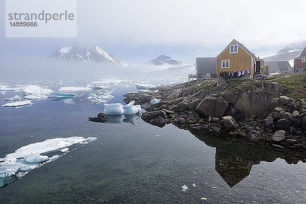 Grönland  Sermersooq  Kulusuk  Holzhütten am Ufer und auf dem Wasser schwimmendes Eis