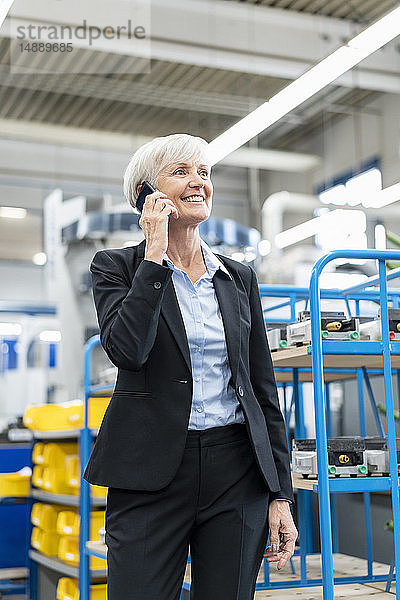 Lächelnde ältere Geschäftsfrau am Handy in einer Fabrik