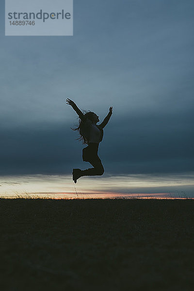 Silhouette einer glücklichen Frau in der Natur  die bei Sonnenuntergang in die Luft springt