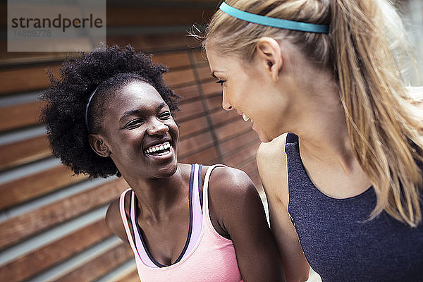 Zwei sportliche junge Frauen unterhalten sich und entspannen sich nach dem Laufen in der Stadt