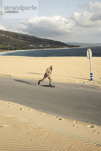 Spanien  Tarifa  Mann in farbenfrohem Anzug fährt Skateboard auf der Straße