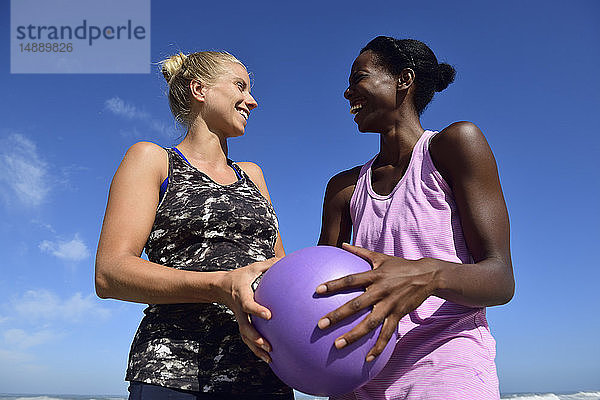 Zwei glückliche Frauen halten Fitnessball unter blauem Himmel