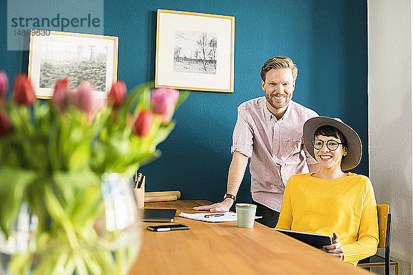 Porträt eines glücklichen Paares an einem Holztisch in ihrem Heimbüro mit einer Tafel in der Hand