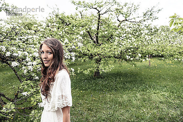 Porträt einer lächelnden jungen Frau im Garten mit blühenden Apfelbäumen