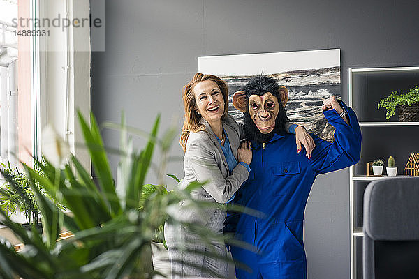 Geschäftsfrau  die mit einem Auszubildenden im Amt steht  mit Affenmaske und blauer Evrall