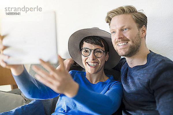 Glückliches Gelegenheitspaar  das im Wohnzimmer ein Selfie mit Tablette einnimmt