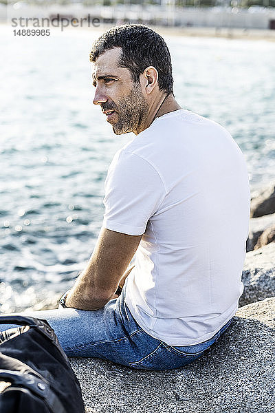 Mann sitzt auf einem Felsen vor dem Meer und entspannt