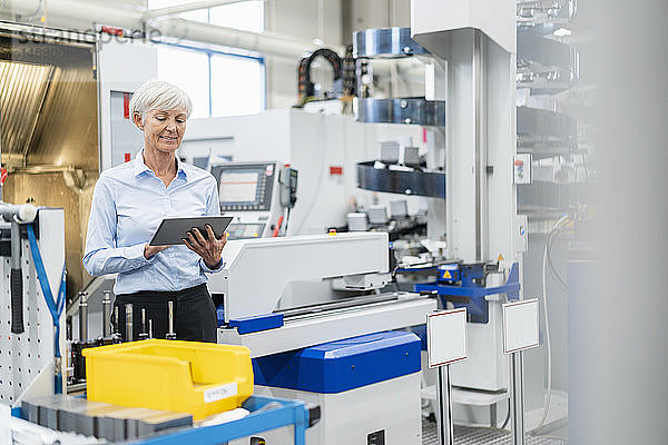 Lächelnde ältere Geschäftsfrau mit Tablette in einer Fabrik