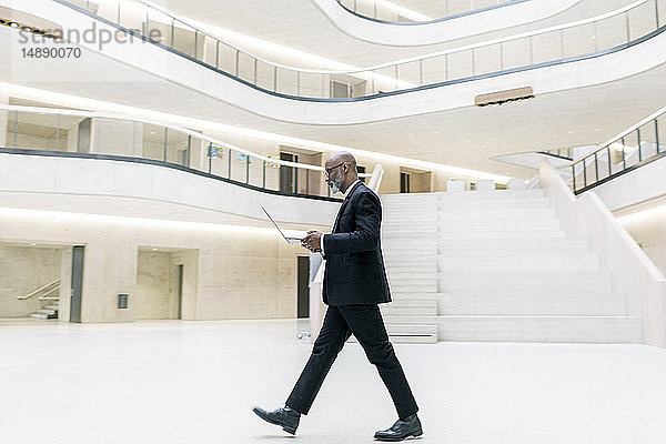 Kluger  reifer Geschäftsmann benutzt Laptop beim Gang durch das Foyer