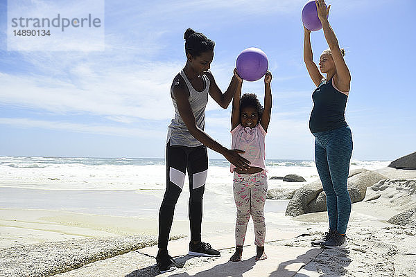 Mutter mit Tochter und Freund trainieren mit einem Ball am Strand