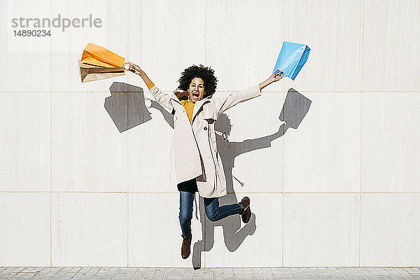 Fröhliche Frau mit Einkaufstüten  die gegen eine Wand springt