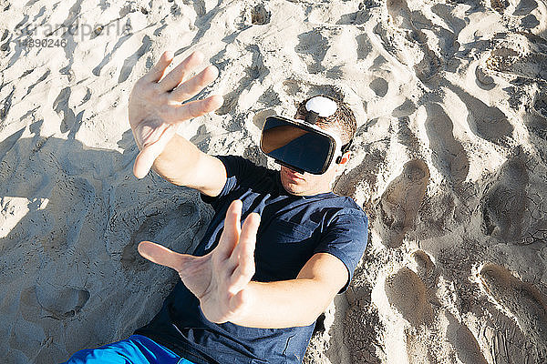 Mann mit VR-Brille liegt im Sand am Strand