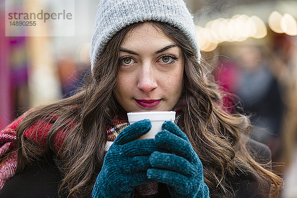 Porträt einer schönen jungen Frau  die auf dem Weihnachtsmarkt ein heißes Getränk hält