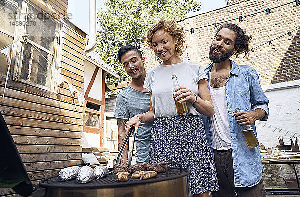 Freunde beim Grillen im Hinterhof  bei der Zubereitung von Fleisch auf dem Grill