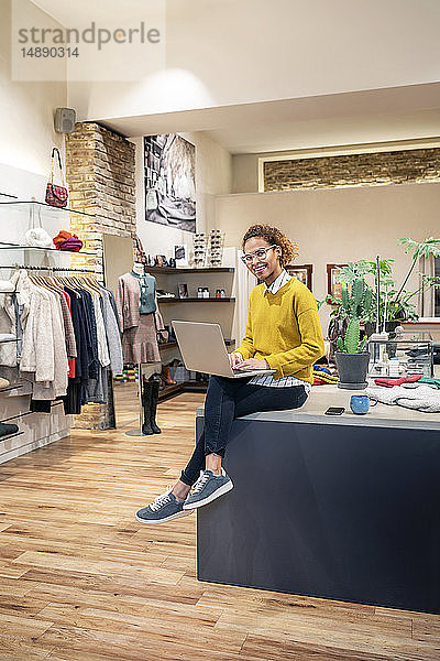 Junge Frau arbeitet in einem Modegeschäft und benutzt einen Laptop