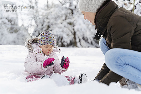 Glückliche Mutter spielt mit Tochter in Winterlandschaft