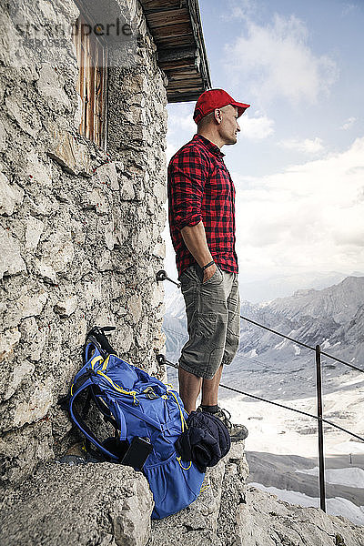 Österreich  Tirol  Mann auf Wanderung  steht an Berghütte und schaut auf Aussicht