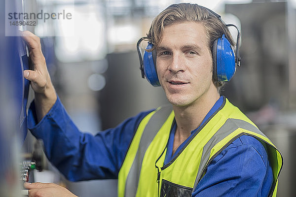 Porträt eines Mannes mit Ohrenschützern bei der Bedienung einer Maschine in einer Fabrik