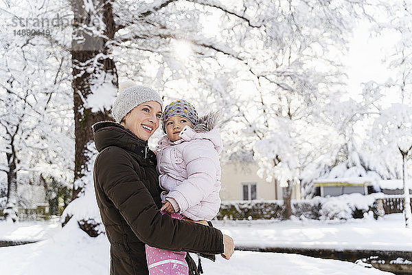 Glückliche Mutter trägt Tochter in Winterlandschaft