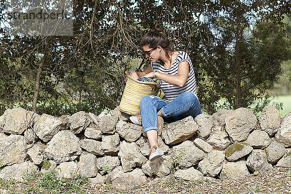 Spanien  Menorca  junge Frau mit Tasche auf Steinmauer sitzend