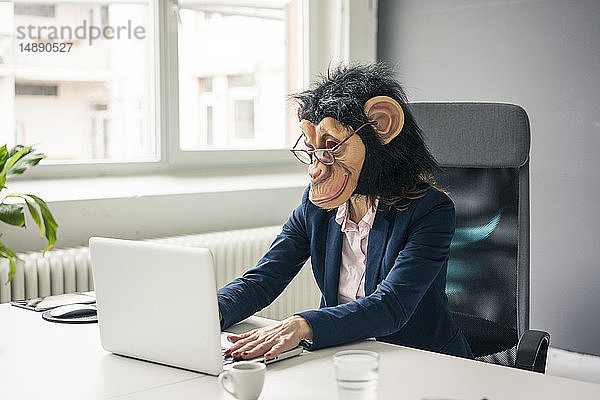 Geschäftsfrau mit Schimpansenmaske  die im Büro arbeitet  mit Laptop