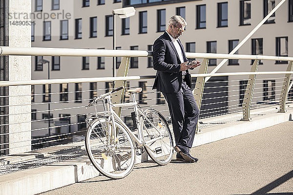 Älterer Geschäftsmann mit Fahrrad und Mobiltelefon in der Stadt