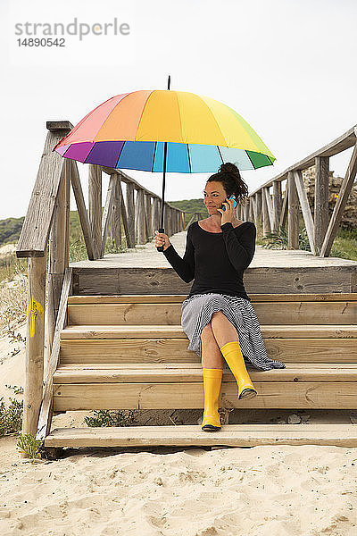 Frau mit buntem Regenschirm am Strand stehend