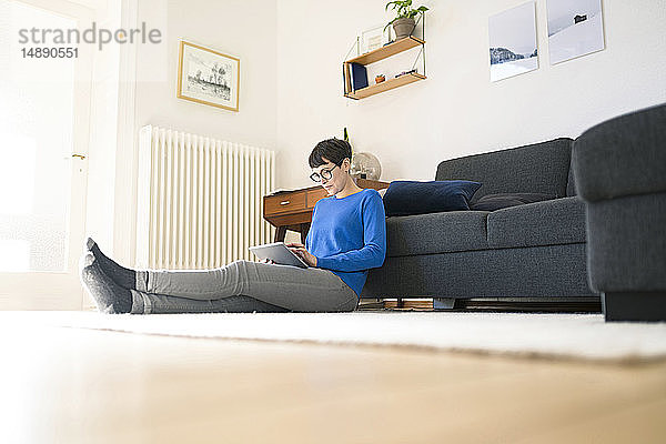 Lässige kurzhaarige Frau entspannt sich im modernen Wohnzimmer mit einer Tablette