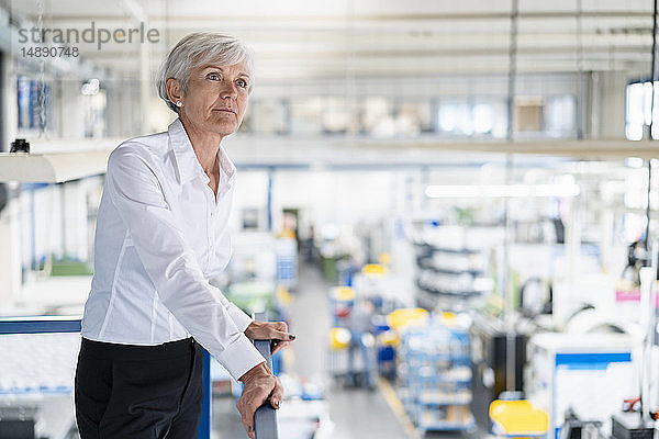 Leitende Geschäftsfrau im oberen Stockwerk einer Fabrik mit Blick auf die Produktionshalle