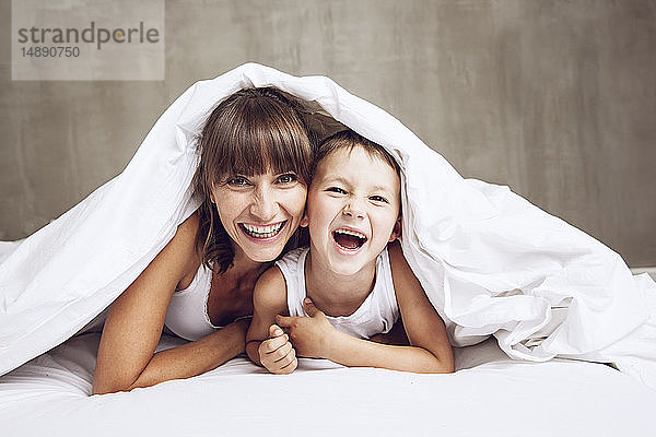 Mutter und Sohn kuscheln unter einer Decke  lachend