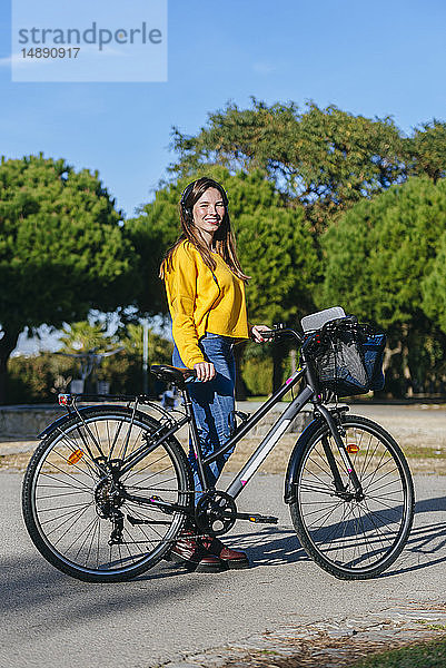 Porträt einer lächelnden jungen Frau mit Fahrrad und Kopfhörer im Park